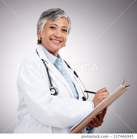 Happy woman, portrait and doctor with clipboard in studio, planning notes or healthcare information. Mature medical worker writing report of insurance checklist, medicine or script on gray background Happy woman, portrait and doctor with clipboard in studio, planning notes or healthcare information. Mature medical worker writing report of insurance checklist, medicine or script on gray background 137466945