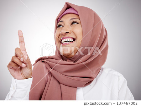 Muslim, thinking and a woman with an idea in studio for happiness, kindness and positive attitude. Hijab, islam and islamic fashion with a mature person on grey background pointing up at announcement 137467002