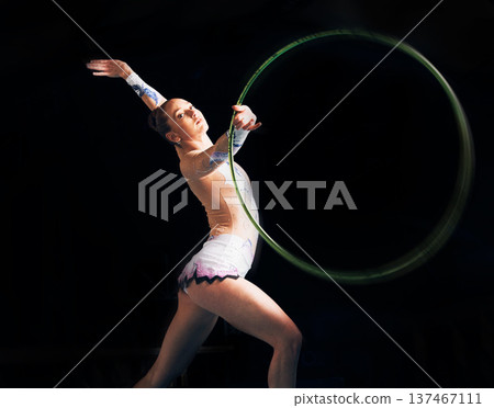 Portrait, training with a gymnastics hoop and a woman in the gym for a performance showcase or practice. Fitness, dance and concert with a female athlete on a dark background for routine or recital Portrait, training with a gymnastics hoop and a woman in the gym for a performance showcase or practice. Fitness, dance and concert with a female athlete on a dark background for routine or recital 137467111