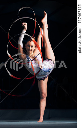 Woman, portrait and balance for ribbon gymnastics, sports performance or competition in dark concert arena. Flexible athlete, dancer and stretching for agile showcase, challenge and rhythm in contest Woman, portrait and balance for ribbon gymnastics, sports performance or competition in dark concert arena. Flexible athlete, dancer and stretching for agile showcase, challenge and rhythm in contest 137467115
