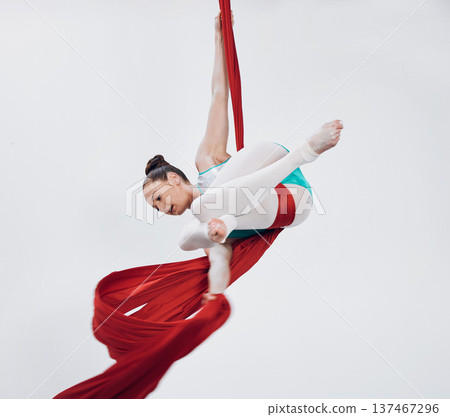 Acrobat, gymnastic and aerial silk with a woman in air for performance, sports and balance. Young athlete person or gymnast hanging on red fabric and white background with space, art and creativity 137467296