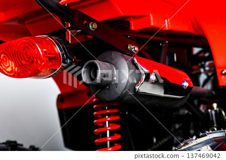 Close up of black exhaust pipe with chrome shield on red atv quad bike with visible rear red suspension spring and brake light for offroad trips 137469042