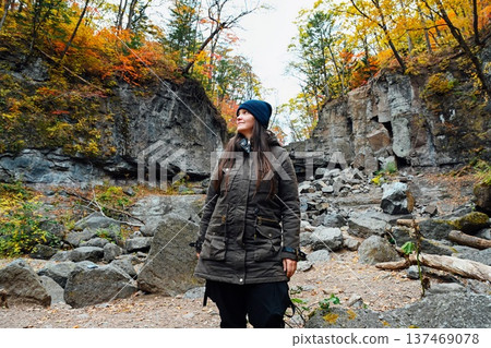 Russian woman solo traveler standing among rocks in autumn forest at Kravtsovskie waterfalls looking aside thoughtful travel nature concept Russian woman solo traveler standing among rocks in autumn forest at Kravtsovskie waterfalls looking aside thoughtful travel nature concept 137469078