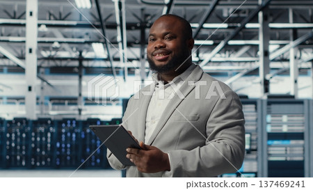 Engineer working in server farm using tablet to analyze data. IT professional examining infrastructure in data center using device, ensuring system integrity and security, camera B Engineer working in server farm using tablet to analyze data. IT professional examining infrastructure in data center using device, ensuring system integrity and security, camera B 137469241