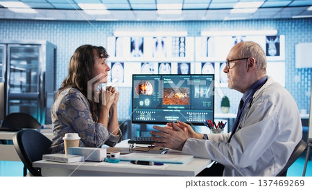 Male oncology specialist reviewing a radiology scan with elderly woman patient, explaining risk factors and preventive options for cancer diagnosis and treatment. Immunotherapy. 137469269
