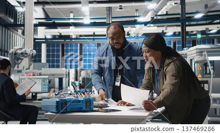 Team of african american consultants reviewing data and checklists in modern solar power facility, ensuring manufacturing process meets sustainable energy and innovation standards. Camera A. Team of african american consultants reviewing data and checklists in modern solar power facility, ensuring manufacturing process meets sustainable energy and innovation standards. Camera A. 137469286