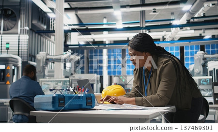 Black engineering expert checking data on papers at the solar energy factory, conducting evaluations of manufacturing systems to ensure production for high tech solar panels. Camera A. Black engineering expert checking data on papers at the solar energy factory, conducting evaluations of manufacturing systems to ensure production for high tech solar panels. Camera A. 137469301