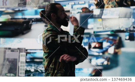 Male army officer operates from a mission command center with digital tech, monitoring satellite intelligence for modern combat strategy. Secure communications in active operations. Camera A. 137469436