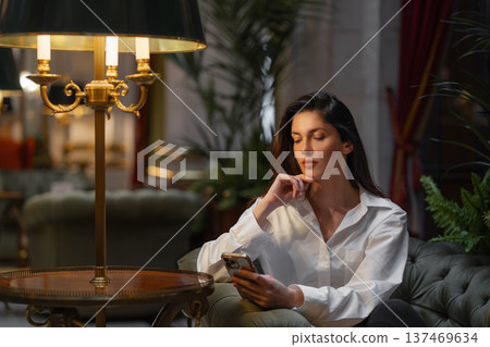 Businesswoman using smartphone on chair near lit Businesswoman using smartphone on chair near lit 137469634