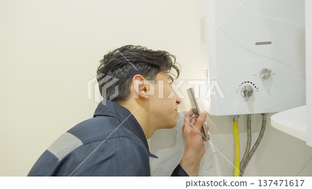 Male technician inspecting a gas water heater in a kitchen 137471617