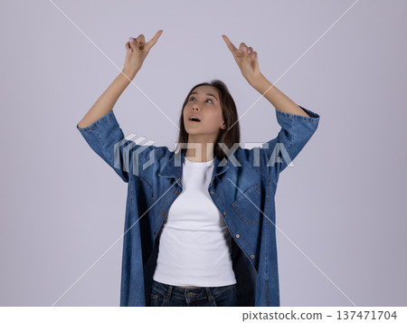 Young woman in blue shirt pointing up with both hands 137471704