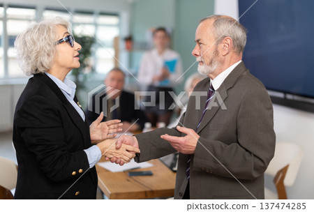 Senior male and female participants of meeting end business negotiations with handshake Senior male and female participants of meeting end business negotiations with handshake 137474285
