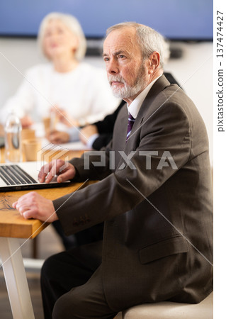 Elderly man in group watches presentation given by young secretary Elderly man in group watches presentation given by young secretary 137474427