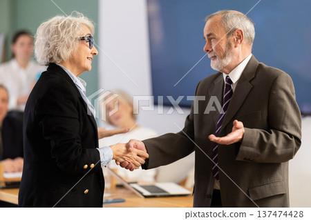 Senior male and female participants of meeting end business negotiations with handshake Senior male and female participants of meeting end business negotiations with handshake 137474428