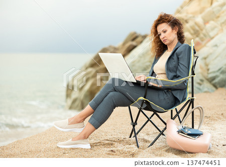 Professional woman seated on a beach chair with a laptop 137474451