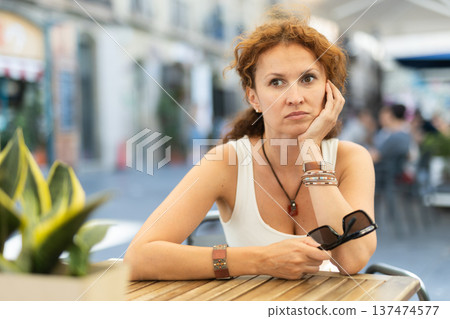 Thoughtful middle-aged woman sitting in open-air cafe Thoughtful middle-aged woman sitting in open-air cafe 137474577