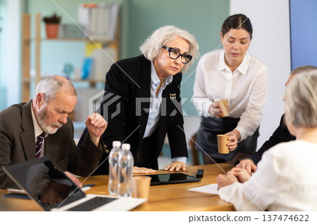 Elderly woman standing and scolding sad senior colleagues at meeting table Elderly woman standing and scolding sad senior colleagues at meeting table 137474622