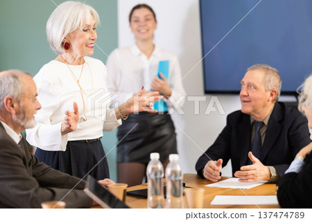 Elderly woman holds meeting while smiling colleagues listen 137474789