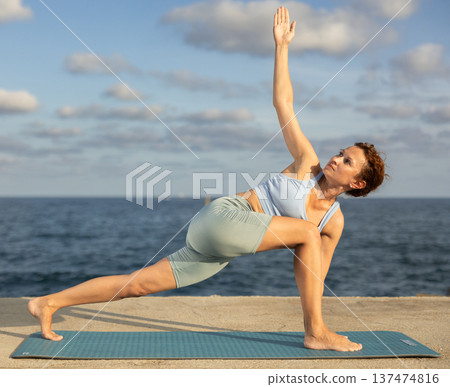 Yoga practice on embankment, female athlete fulfil carry out Parivritta Parshvakonasana 137474816
