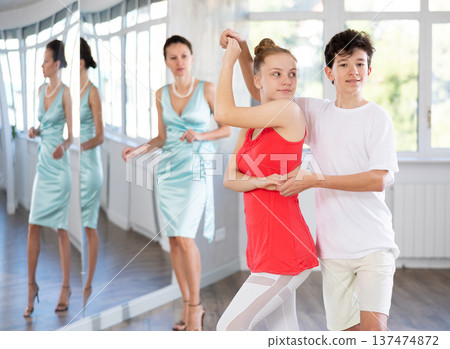 Couple of teenage dancers rehearsing ballroom dance with female teacher Couple of teenage dancers rehearsing ballroom dance with female teacher 137474872