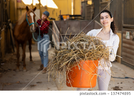 Young woman with bucket of hay in stable 137474895