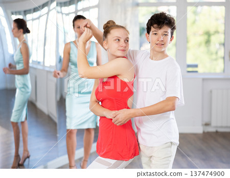 Experienced dance teacher teaching ballroom dancing to a couple of teenagers in studio 137474900