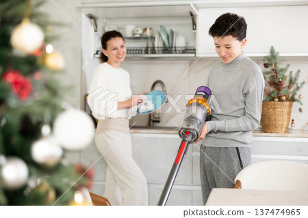 Mother and her teenage son are preparing to celebrate Christmas at home - they are cleaning kitchen, vacuuming floor and washing dishes 137474965