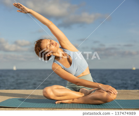 Yoga practice on embankment, female athlete fulfil carry out padmasana svastikasana, Siddhasana 137474989
