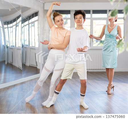 Experienced dance teacher teaching ballroom dancing to a couple of teenagers in studio 137475060