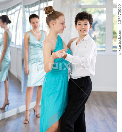 Girl and a boy in festive clothes learn to dance tango under guidance of teacher 137475090