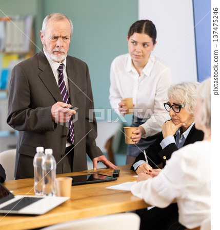 Elderly man standing and scolding sad senior colleagues at meeting table 137475246