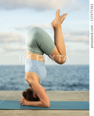 Yoga practice on embankment, female athlete fulfil carry out shirshasana Yoga practice on embankment, female athlete fulfil carry out shirshasana 137475363
