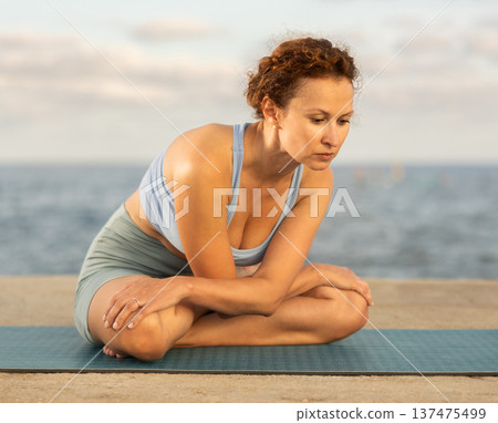 Yoga practice on embankment, female athlete fulfil carry out padmasana svastikasana, Siddhasana 137475499