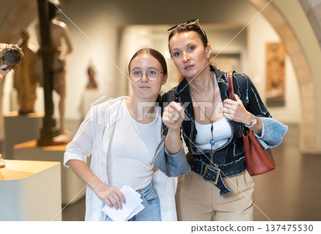 Young woman with teen daughter walk around museum, view sculpture in museum hall 137475530
