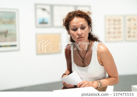 Thoughtful woman examining photographs on walls in art gallery Thoughtful woman examining photographs on walls in art gallery 137475533