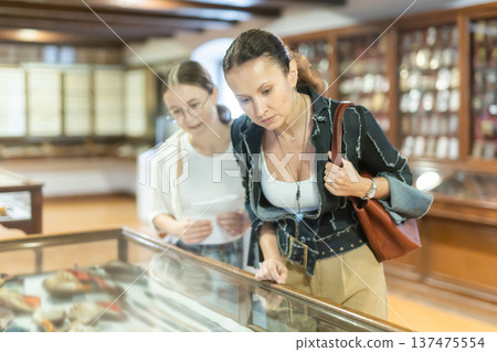 Young woman with teen daughter visitors stands near horizontal glass display case 137475554