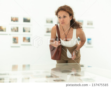 Middle-aged woman looking at objects under showcase in museum Middle-aged woman looking at objects under showcase in museum 137475585