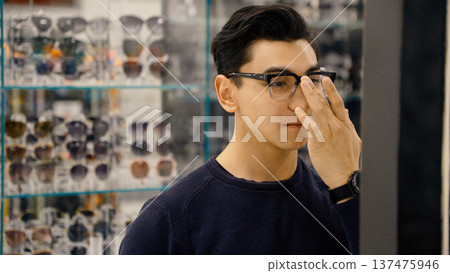 Man adjusting eyewear frame while looking at mirror in shop 137475946
