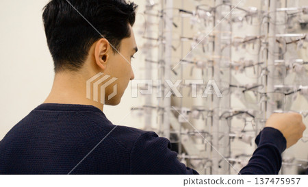 Side view of man examining eyeglasses on display in optic store Side view of man examining eyeglasses on display in optic store 137475957