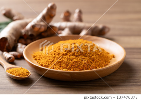 Turmeric powder in a wooden bowl with a wooden spoon and fresh turmeric roots Turmeric powder in a wooden bowl with a wooden spoon and fresh turmeric roots 137476375