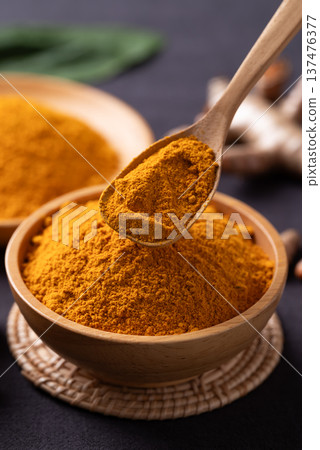 Turmeric powder in a wooden bowl with a wooden spoon scooping it Turmeric powder in a wooden bowl with a wooden spoon scooping it 137476377
