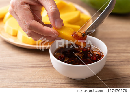 Hand dipping sliced mango into Thai sweet fish sauce (Nam Pla Wan) 137476378