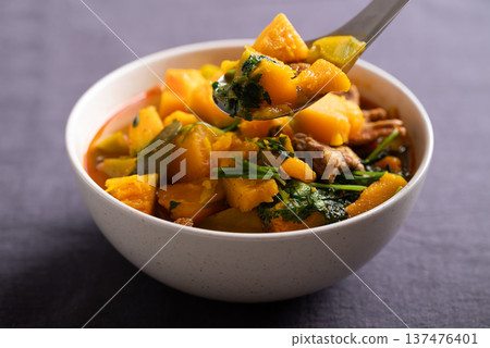 Thai spicy pumpkin curry soup with pork in a bowl scooping by spoon and eating 137476401