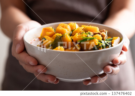 Thai spicy pumpkin curry soup with pork in a bowl holding by hand and serving 137476402