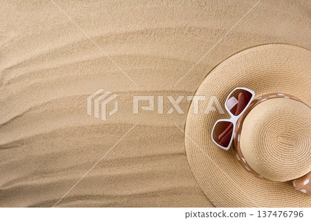 Women's summer straw hat with ribbon and sunglasses on a beach sand, top view. 137476796