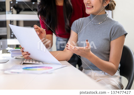 Close up of smiling asian woman holding document explaining to friend or coworker at table in office Close up of smiling asian woman holding document explaining to friend or coworker at table in office 137477427
