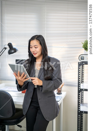 Asian businesswoman or office worker looking at tablet in surprised while standing at computer table 137478586