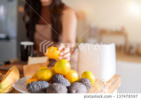 Close up of woman with coffee mug holding orange aside toaster standing at kitchen cooking counter. Close up of woman with coffee mug holding orange aside toaster standing at kitchen cooking counter. 137478597