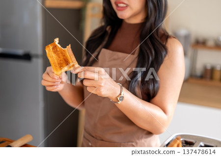 Close up of woman in apron holding and looking at burnt bread in disgusted while standing in kitchen 137478614