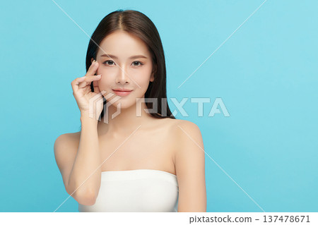 A beautiful young Asian woman with clean, fresh skin against a blue background. Skincare, facial treatment, cosmetology, beauty, and spa. An elegant portrait of an Asian woman. 137478671